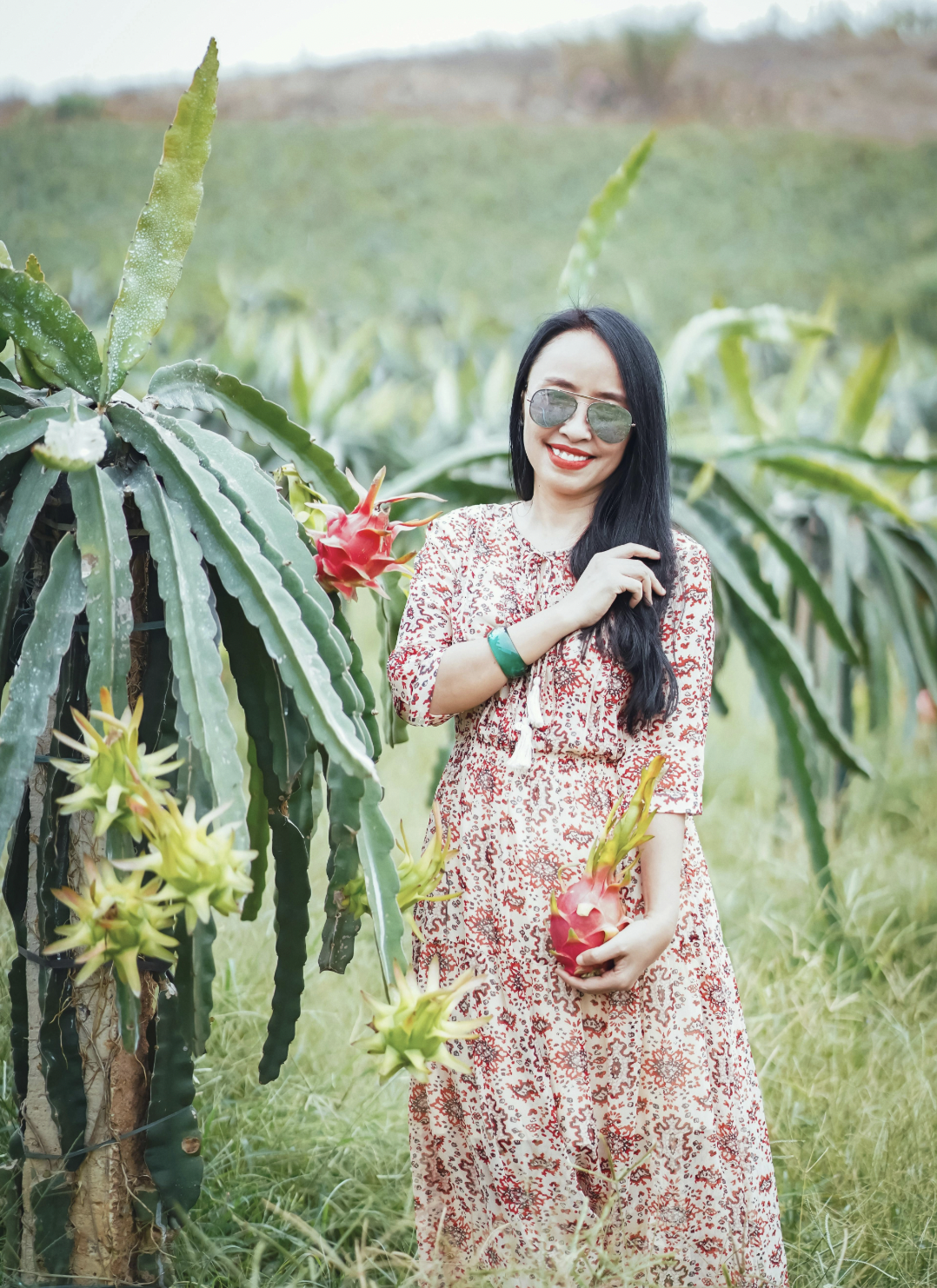 Smiling woman holding dragon fruit in a lush green farm | Lan Anh Hoàng
