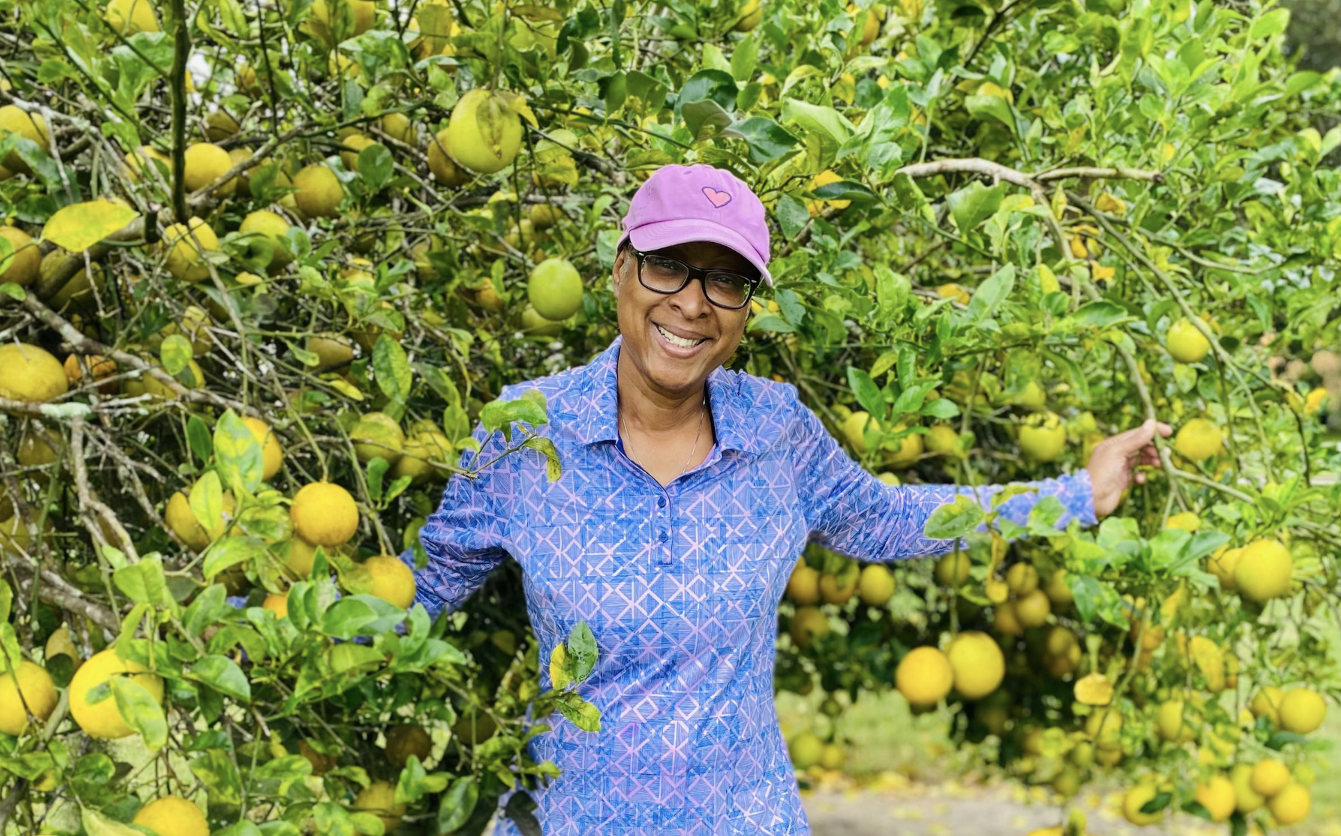 A joyful woman in a cap smiles surrounded by a well pruned meyer lemon trees in Florida